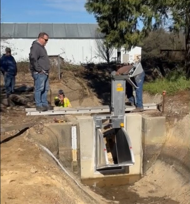 A group of people working on a water management system near a concrete structure with a water gate or valve.