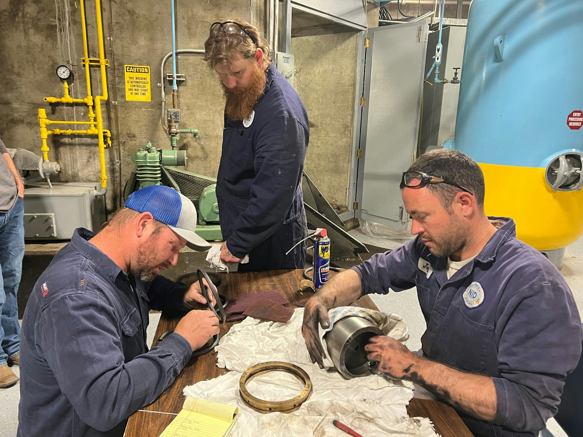 Three workers in an industrial setting, possibly inspecting or repairing equipment.