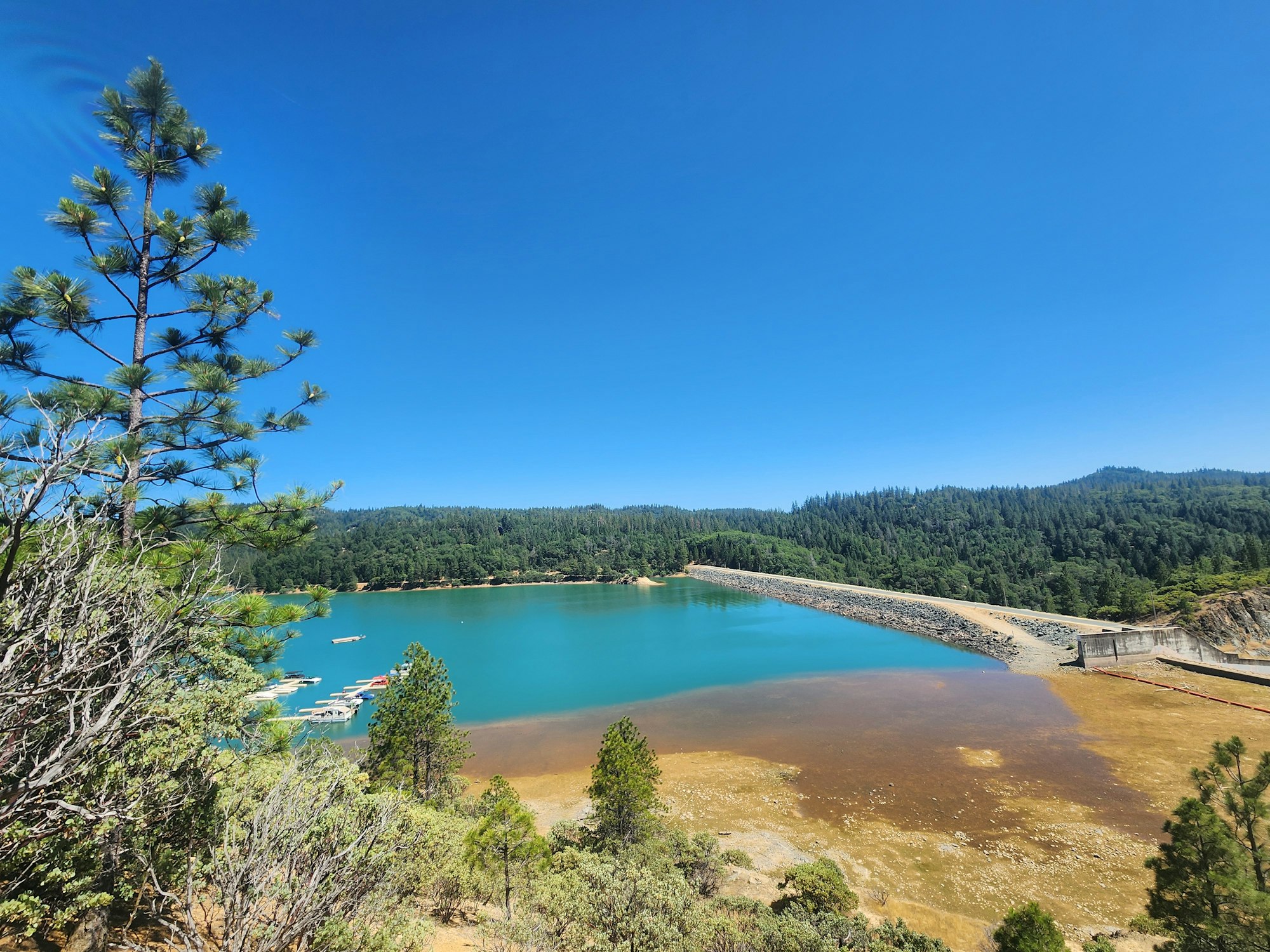 A scenic view of a lake, dam, trees, and a clear blue sky.