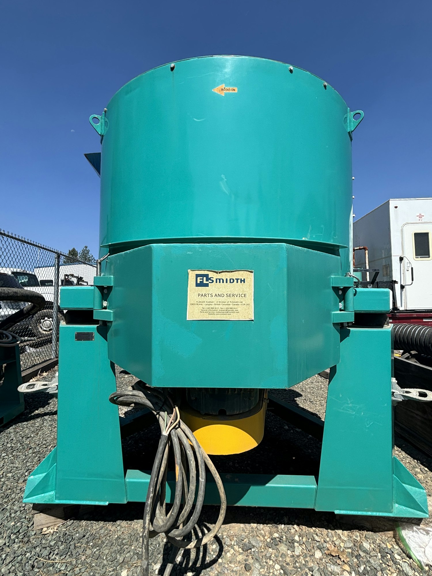 The image shows a large, teal industrial machine with a yellow base and visible electrical cables, likely used for processing.