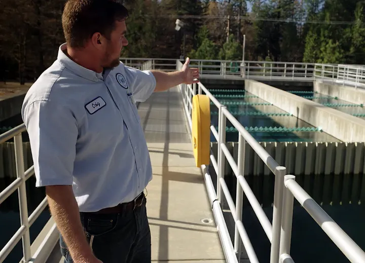 A man in a work shirt is gesturing at water treatment facilities, highlighting the process or equipment in use.