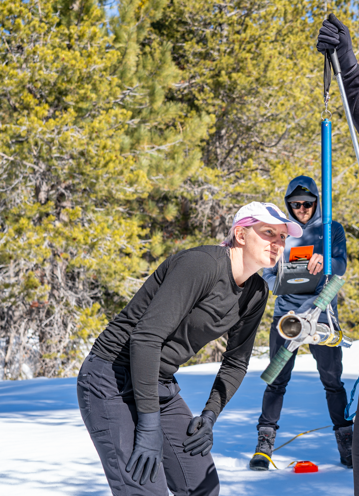 Two people working with equipment in a snowy forest setting.