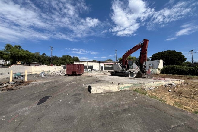A demolition site with an excavator and a dumpster under a clear sky.