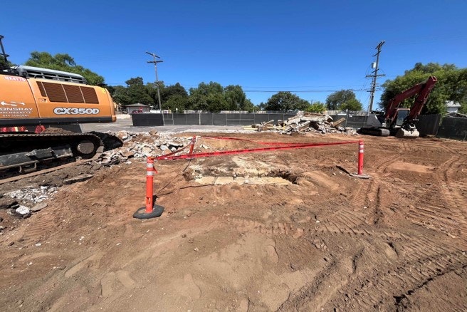 Construction site with excavator, rubble, and barrier.