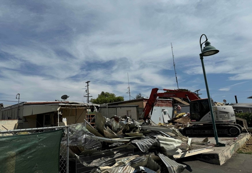 Demolition site with excavator and debris under blue sky.