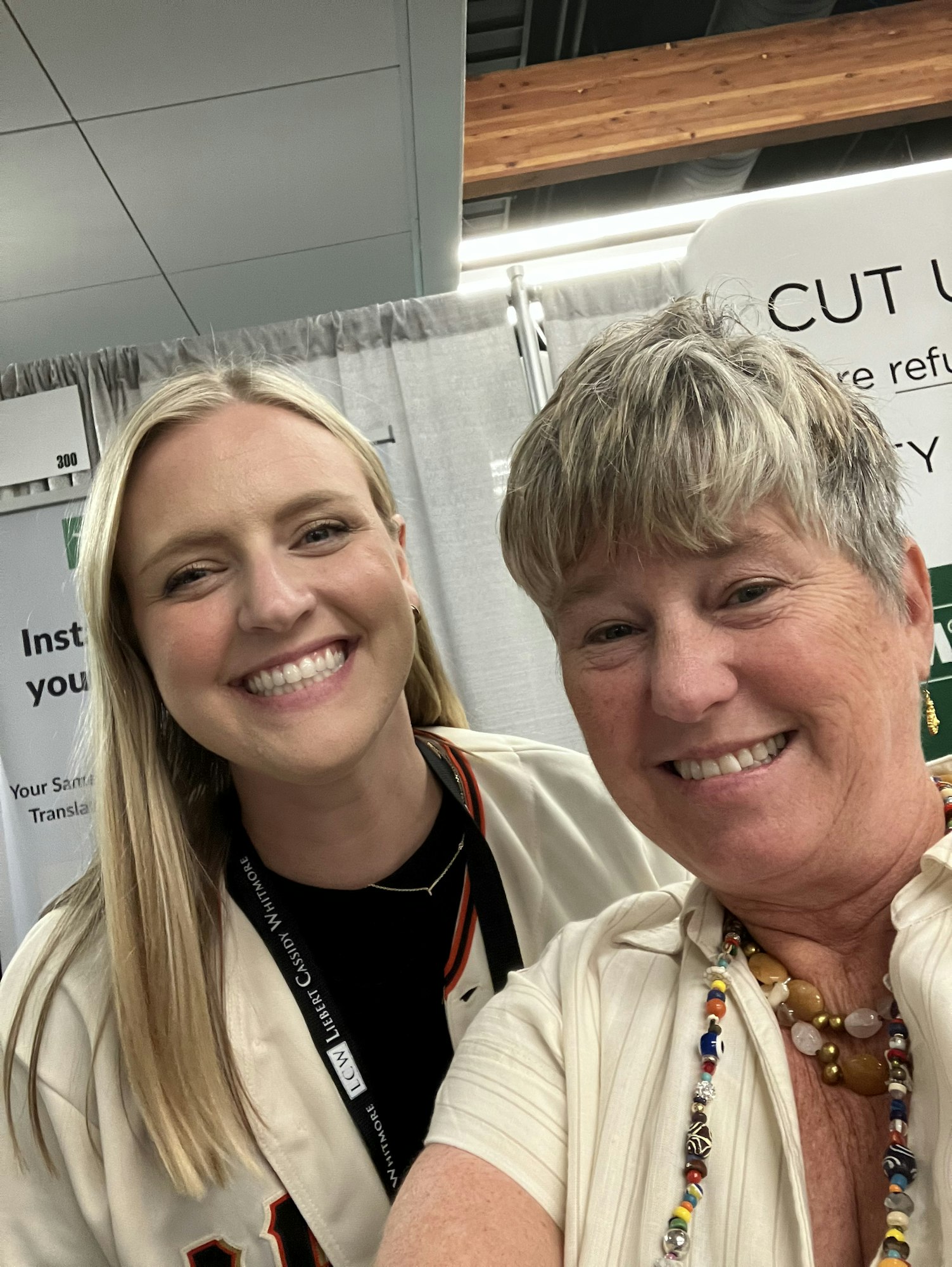 Two people smiling for a selfie at an event with a partial sign in the background.