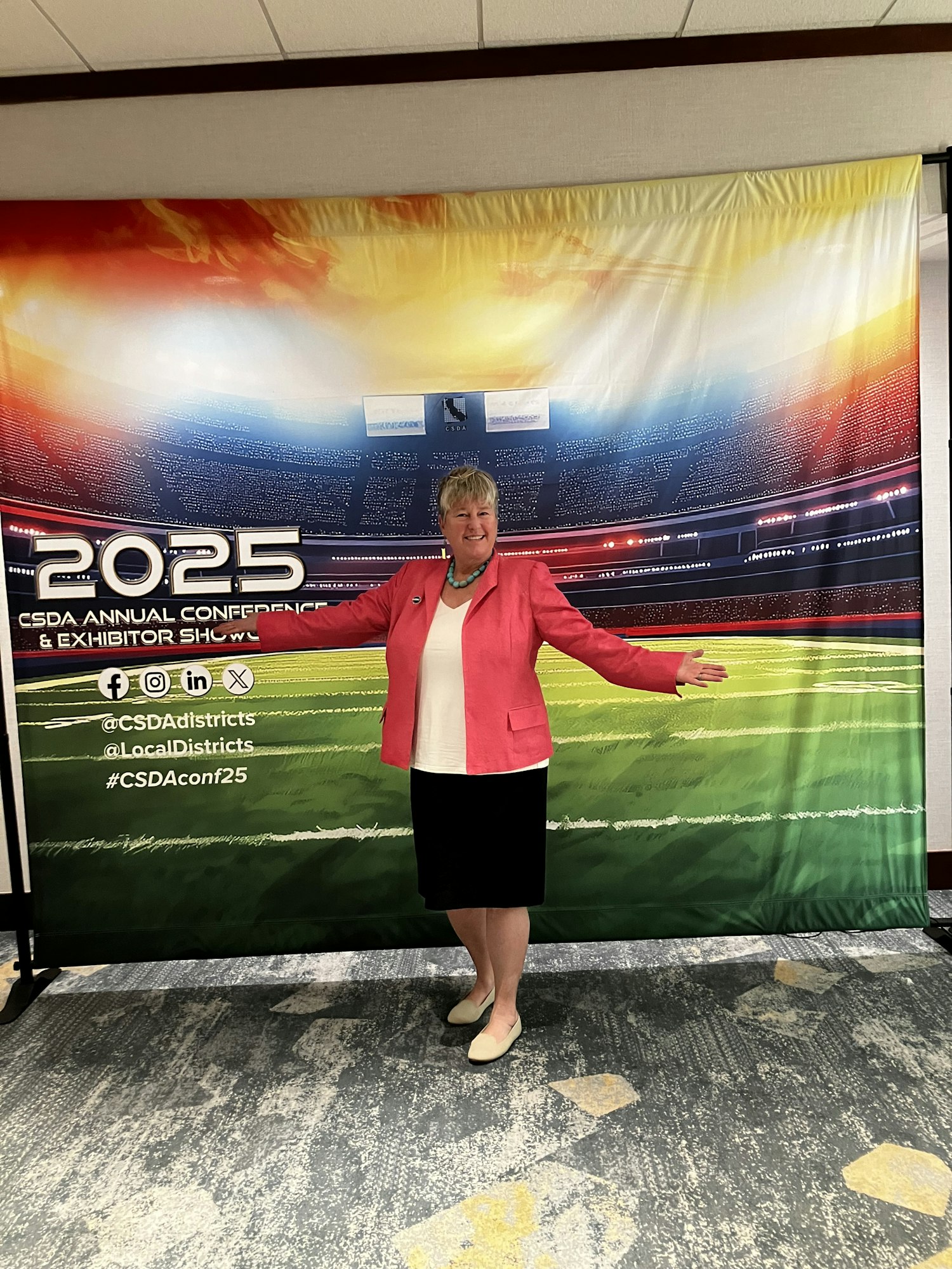 A person poses with open arms in front of a colorful backdrop for the 2025 CSDA Annual Conference & Exhibition Showcase.