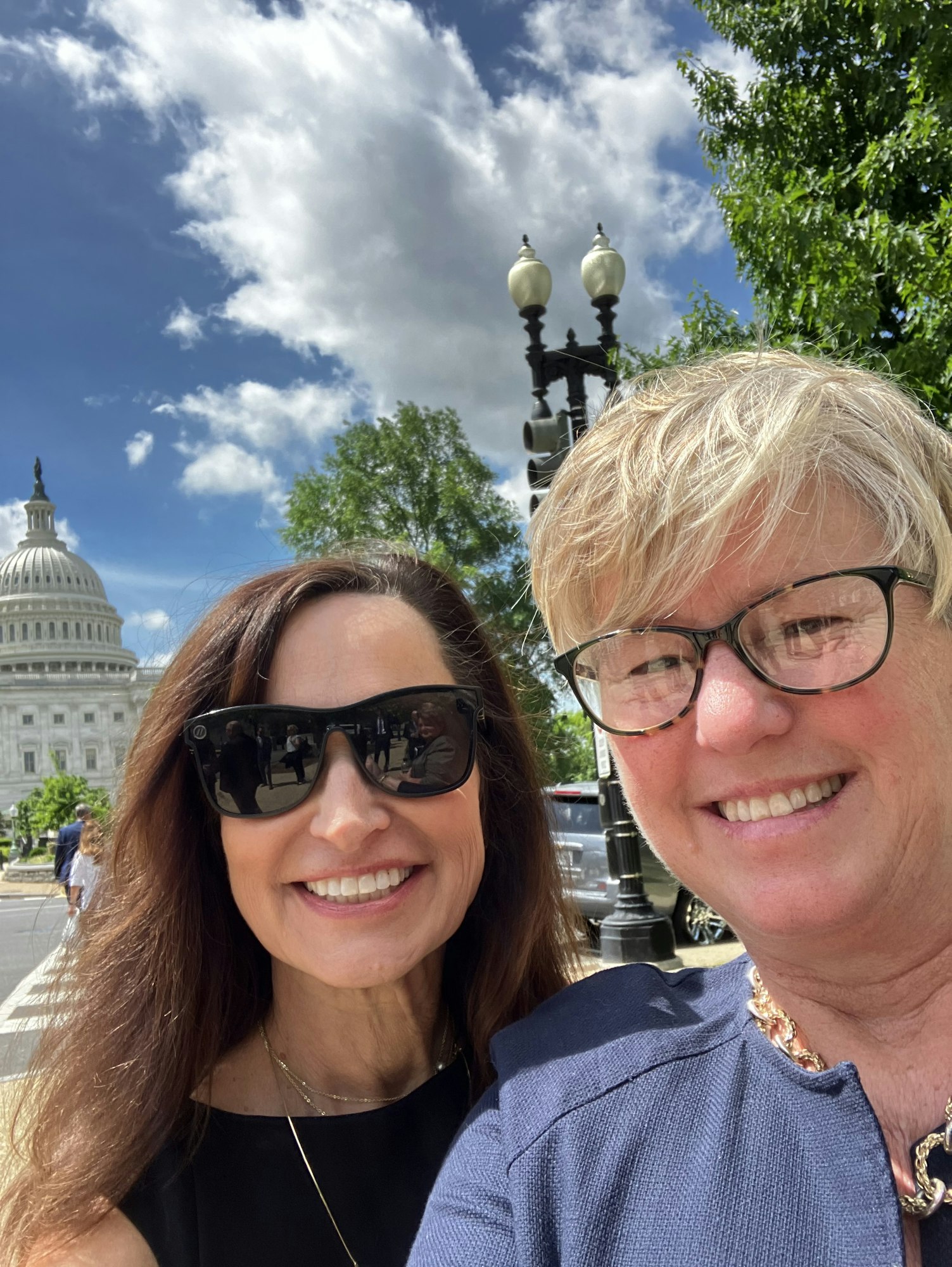 Two people smiling in front of the U.S. Capitol on a clear day.