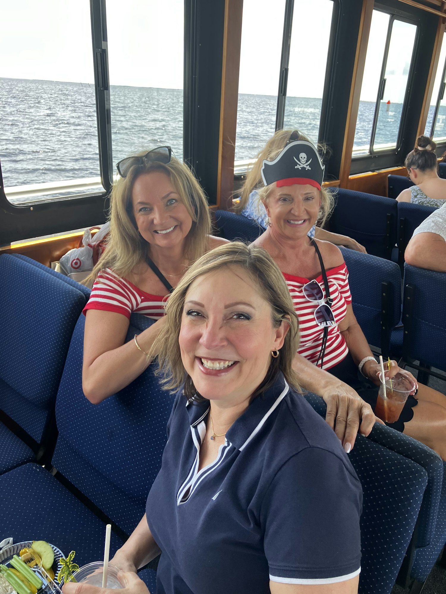 Three women smiling on a boat, one wearing a pirate hat.