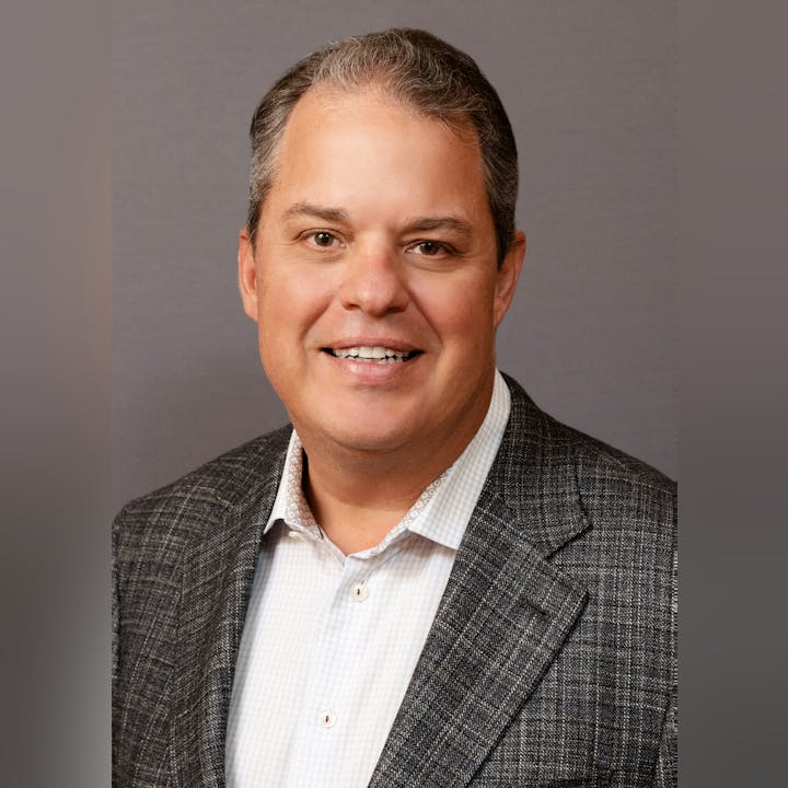 A professional headshot of a smiling person in a blazer and collared shirt.