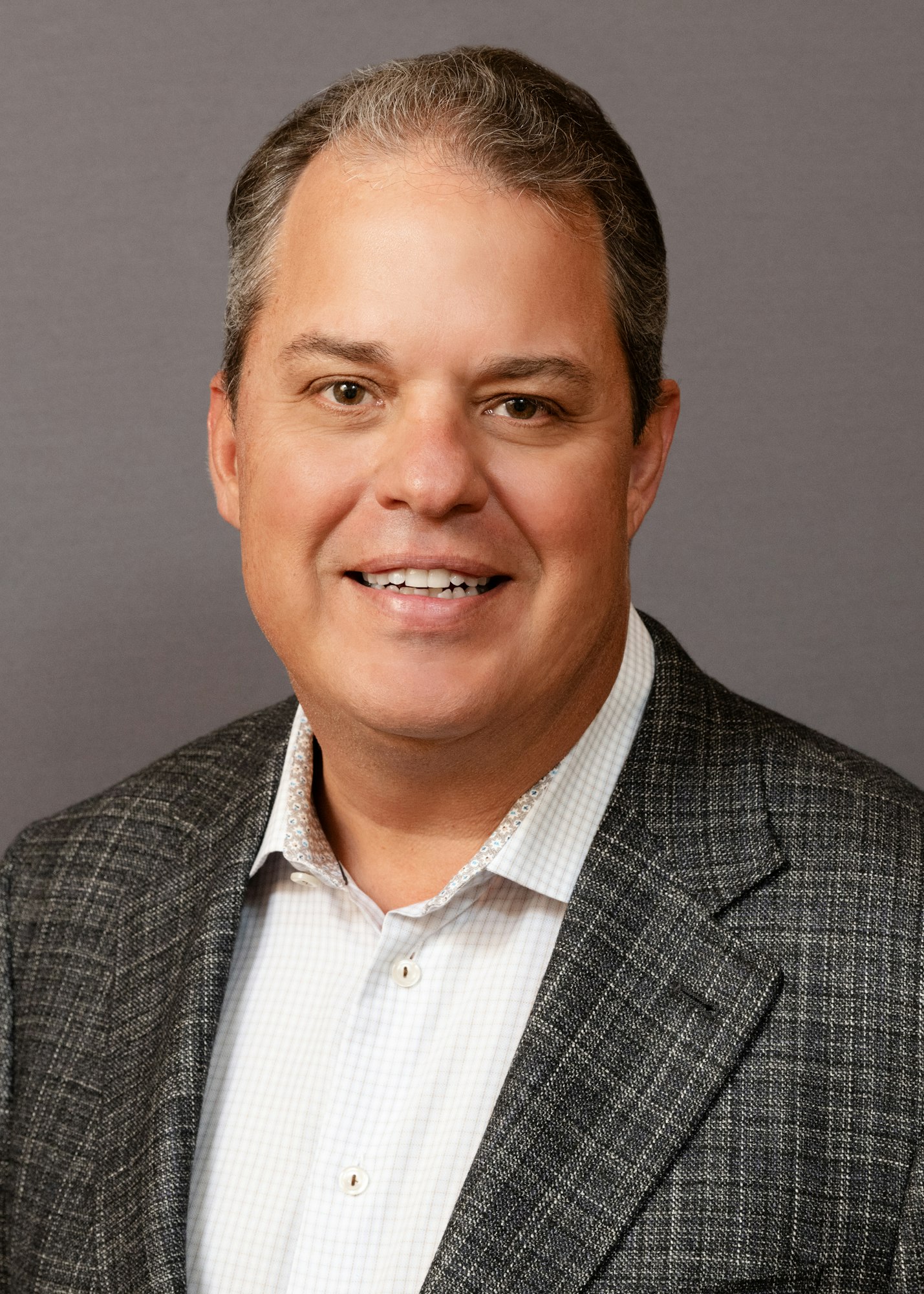 A professional headshot of a smiling person in a blazer and collared shirt.
