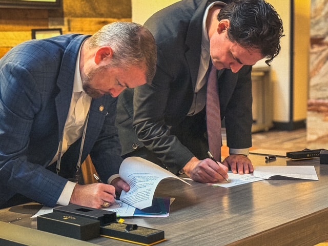 Two men in suits are signing documents on a desk.