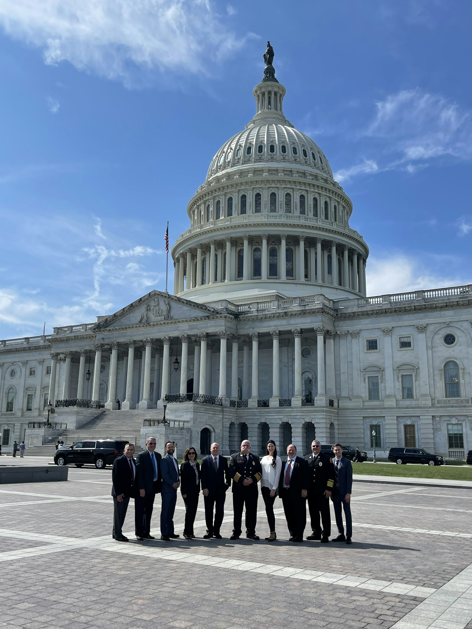 A group poses for a photo in front of the U.S. Capitol building on a sunny day.
