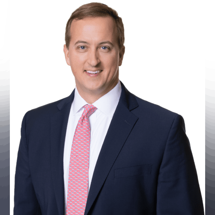 A smiling man in a suit with a red tie against a green background.