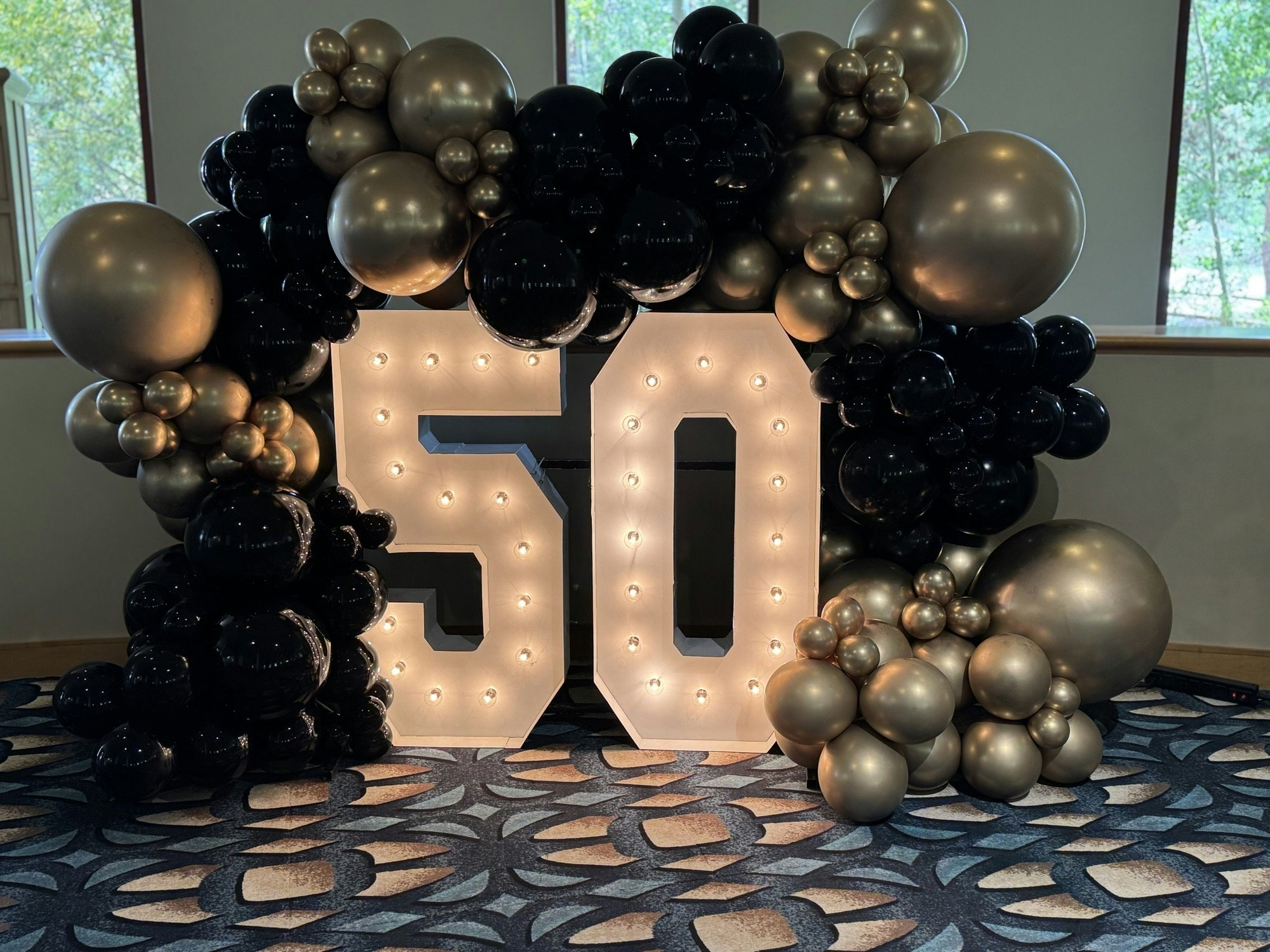 A large light-up "50" surrounded by black and gold balloons in a decorative arrangement.