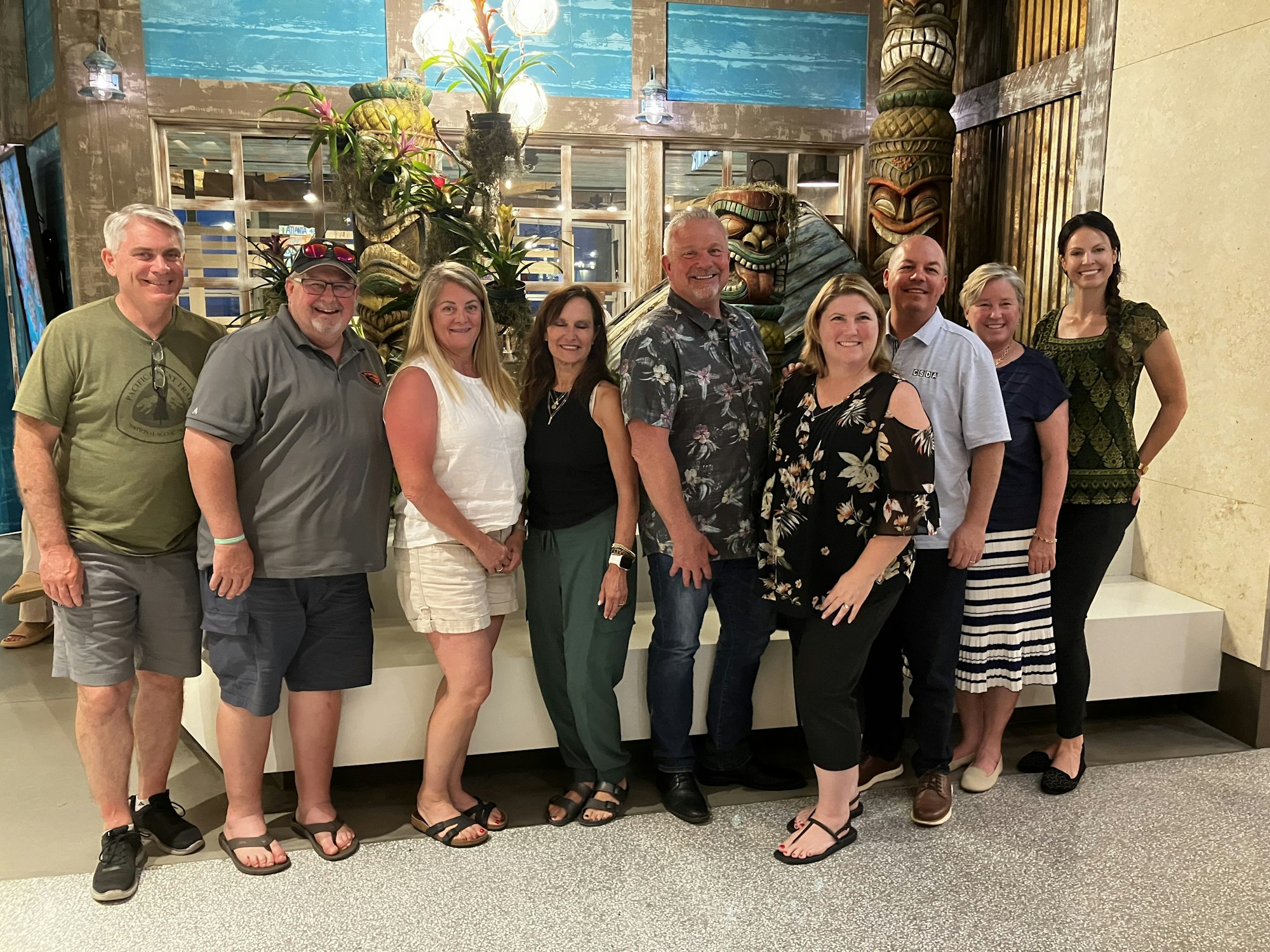 A group of nine people posing indoors in front of a decorative background, smiling.