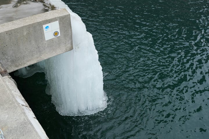 A frozen waterfall or ice formation on a concrete structure next to a water body.
