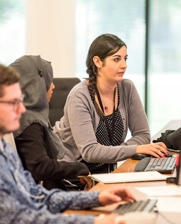 Three individuals in a meeting, one using a keyboard, in a brightly lit room.