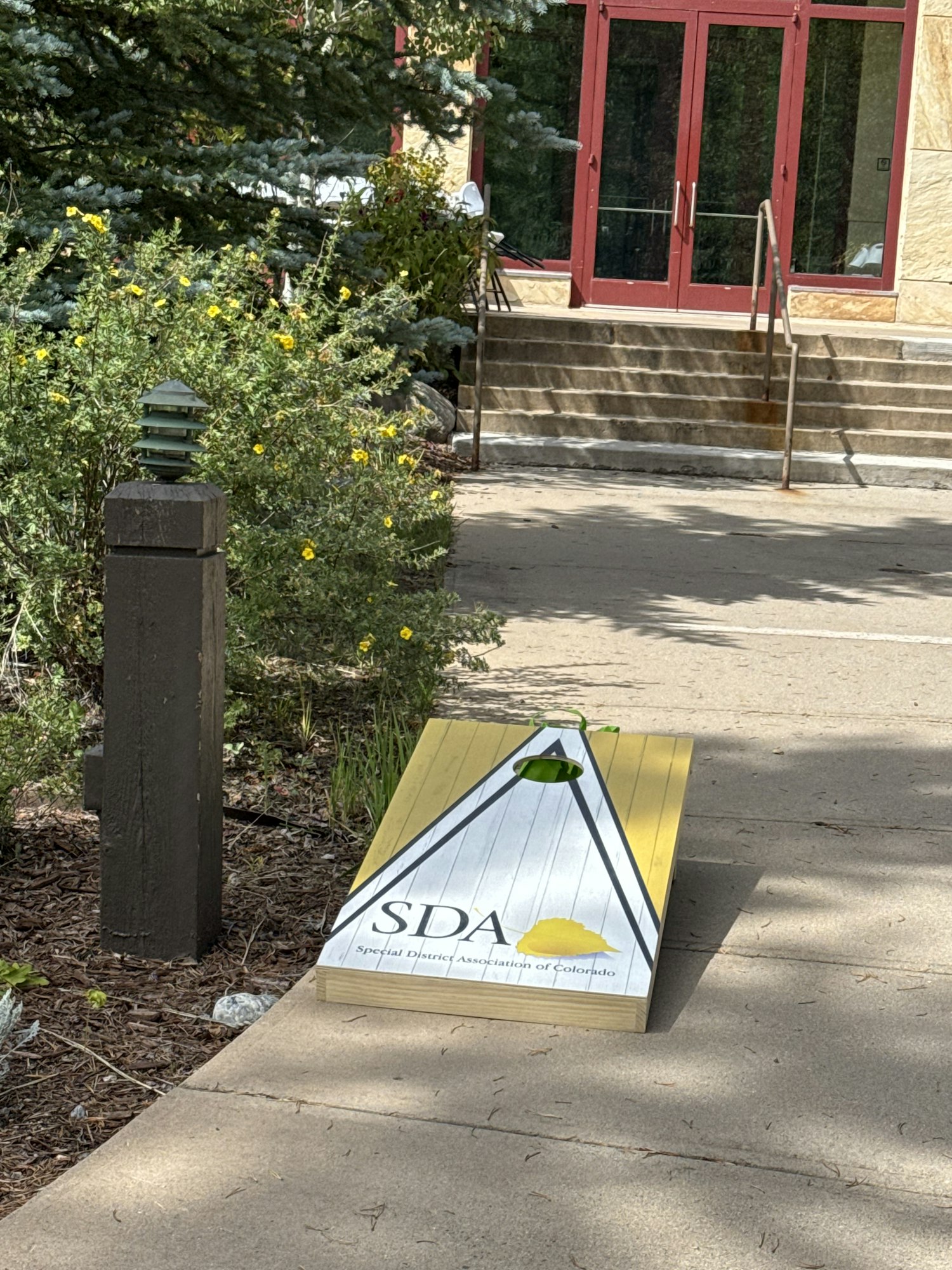 A bean bag toss board with "SDA" and steps leading to a building.