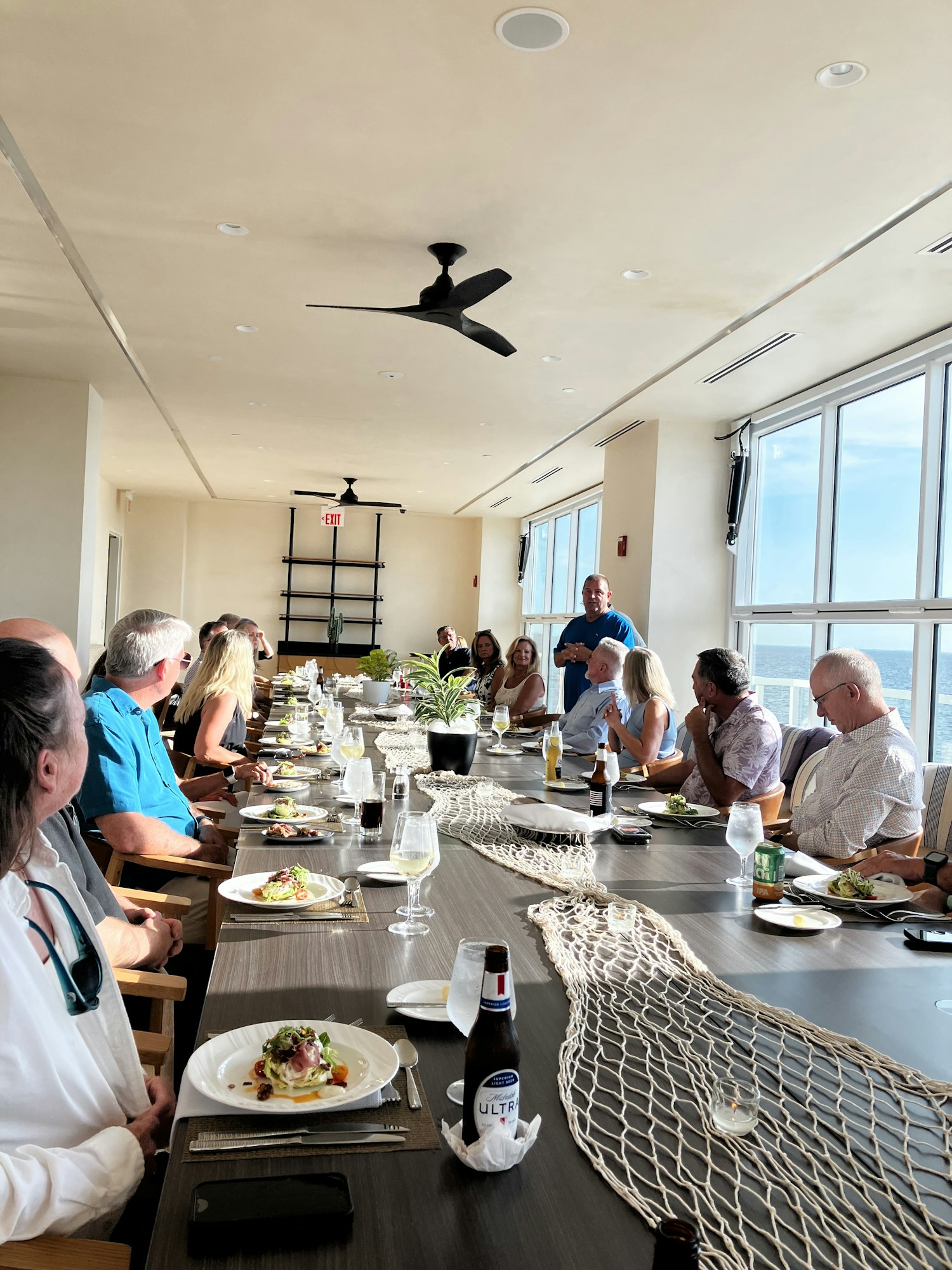 People sitting around a long table with food and drinks in a bright room with skylights.
