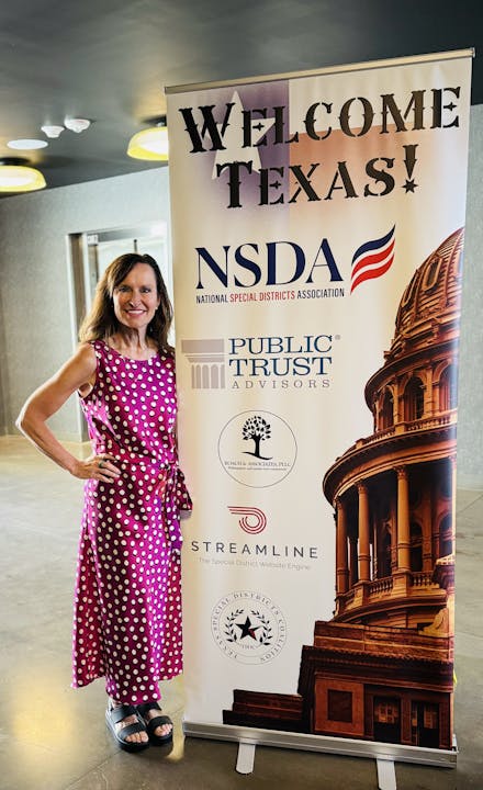 A woman in a pink dress stands next to a "Welcome Texas!" banner with NSDA, Public Trust, and Streamline logos.