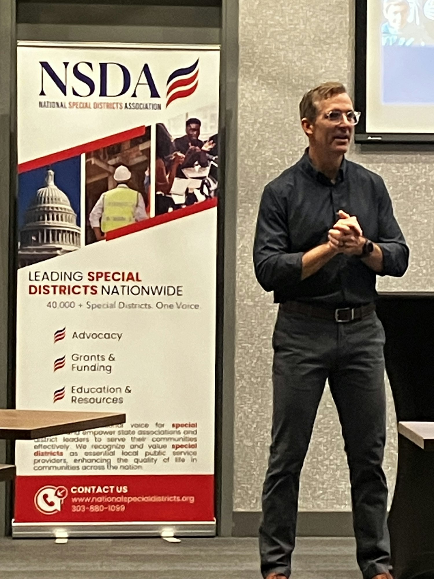 A person standing next to an NSDA banner in a conference room.