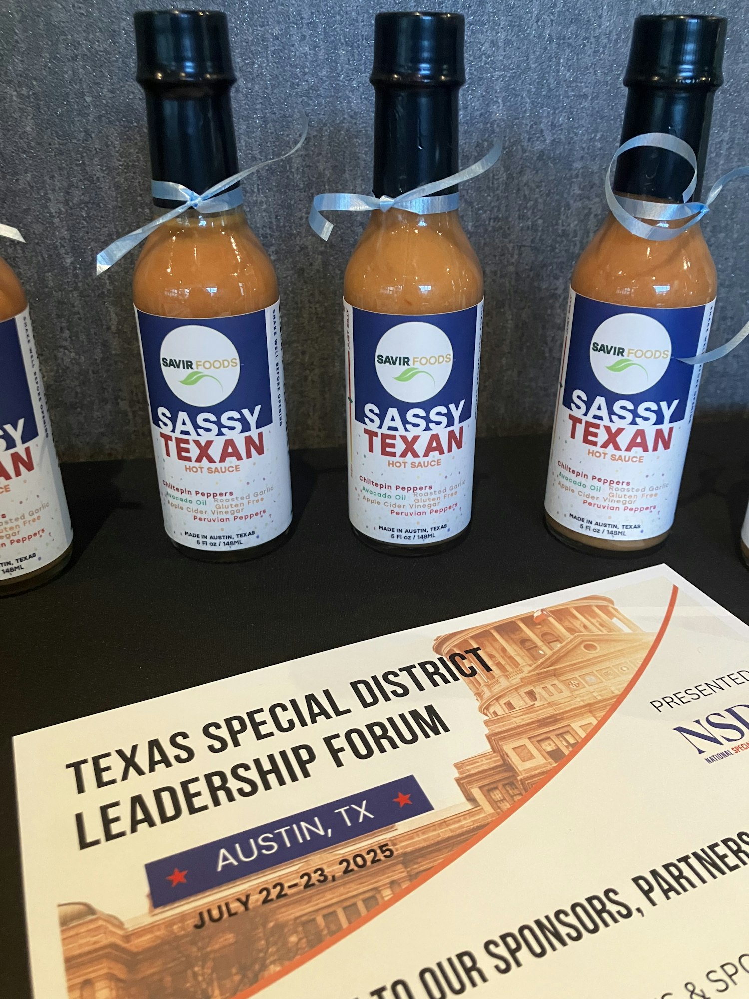 Bottles of "Sassy Texan" hot sauce and a flyer for the Texas Special District Leadership Forum in Austin, TX.