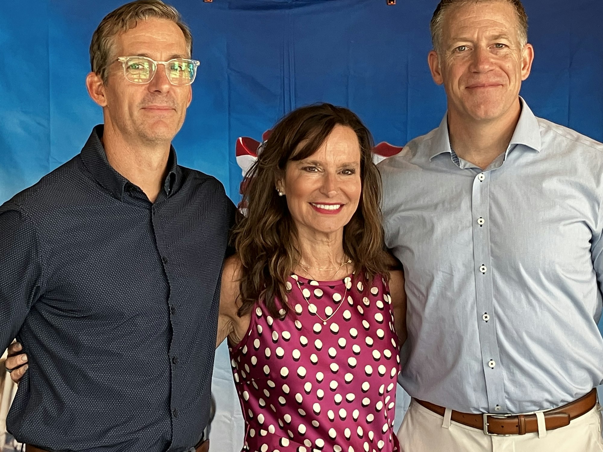 Three adults posing and smiling in front of a blue and red backdrop.