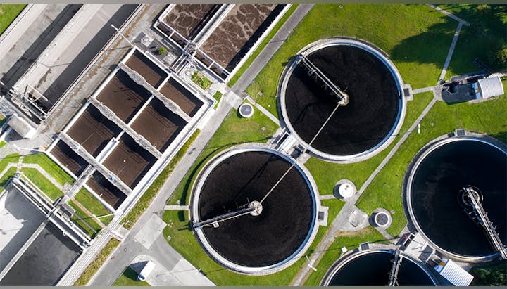 An aerial view of a wastewater treatment facility with circular tanks and rectangular sections, showing the treatment process.