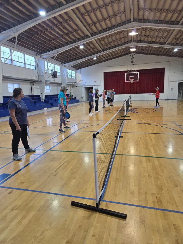 People are lined up in a gymnasium, holding paddles, likely preparing to play pickleball.