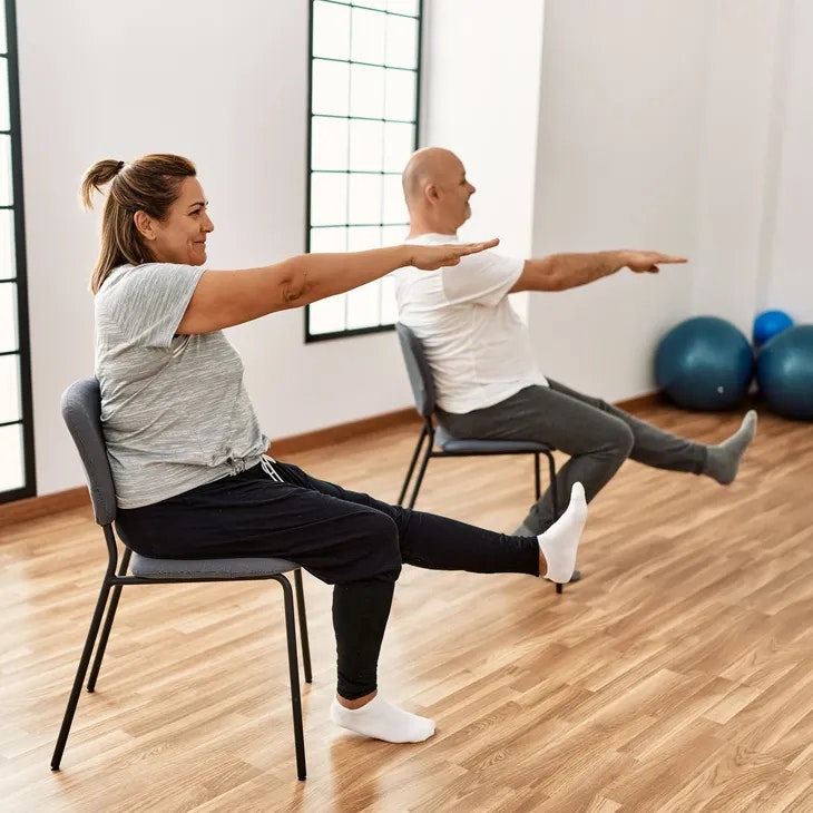 Two people doing seated exercises on chairs in a room with exercise balls.