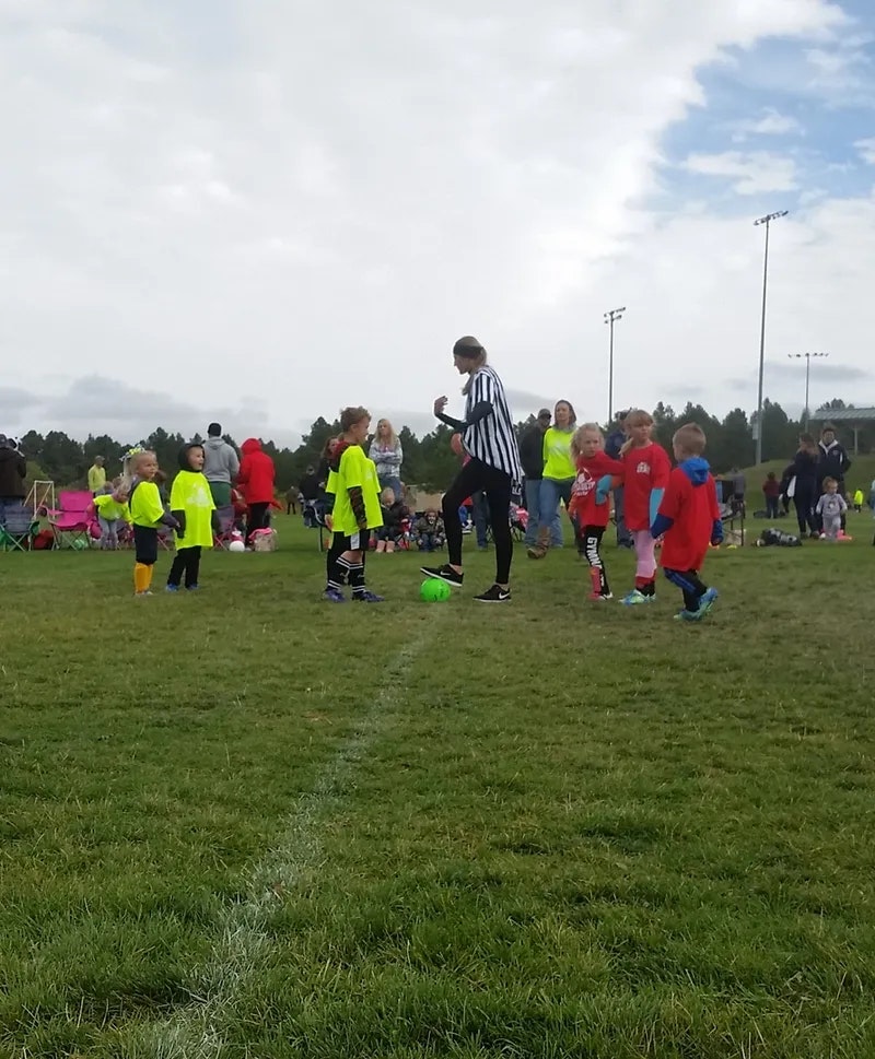 Kids in brightly colored jerseys on a soccer field, with a referee nearby.