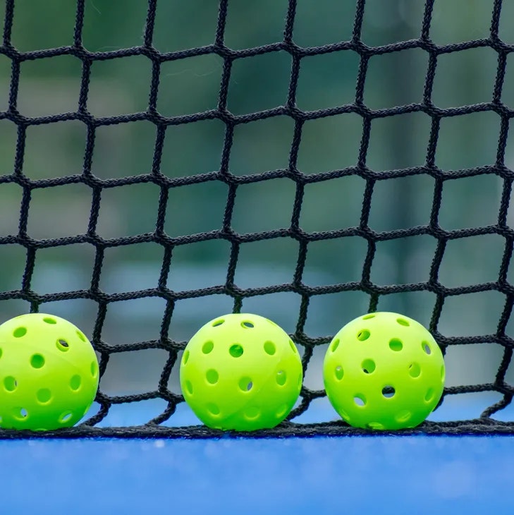 Three green perforated balls in front of a black net on a blue surface.