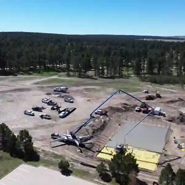 Construction site with cement work, several trucks, and equipment in a forested area.