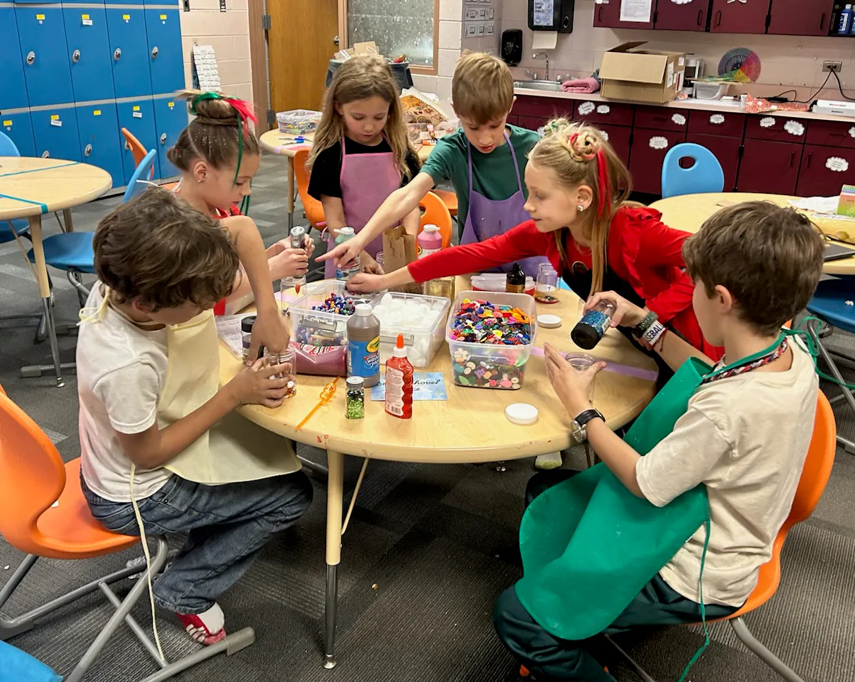 A group of children is engaged in a creative activity at a table, working with colorful materials and craft supplies.