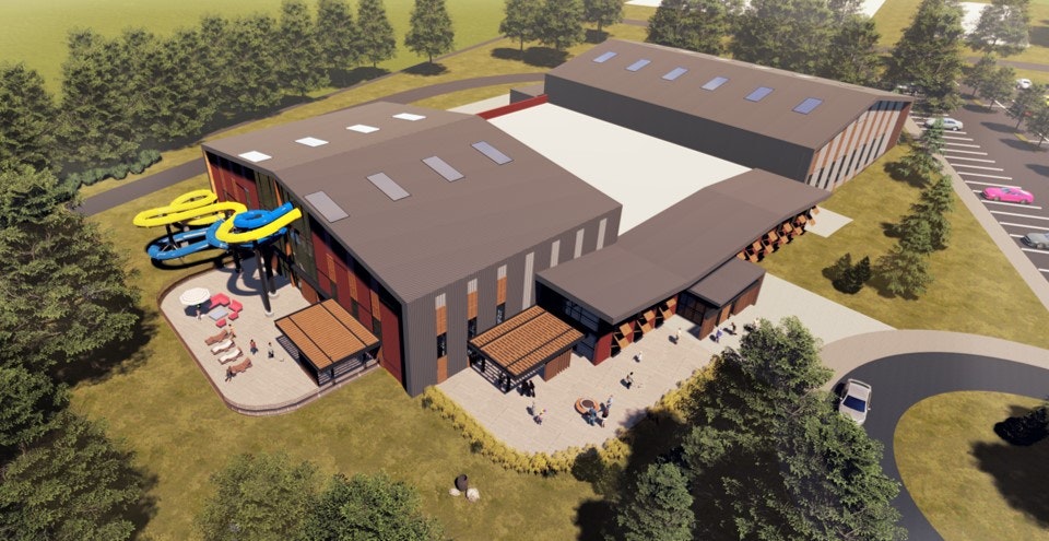 Aerial view of a modern building with colorful waterslides, outdoor seating, surrounded by trees and a parking area.