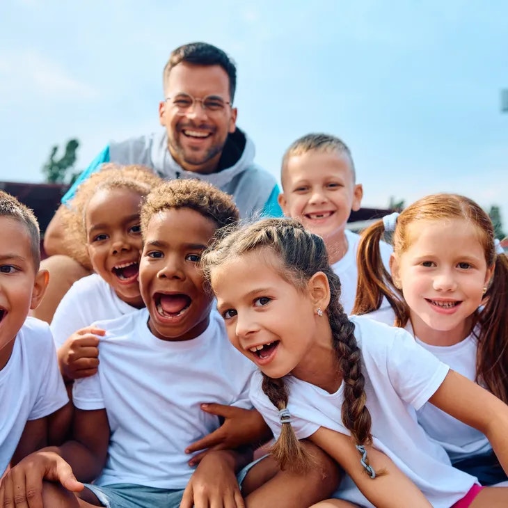 A smiling group of children and an adult outside, all wearing white shirts.