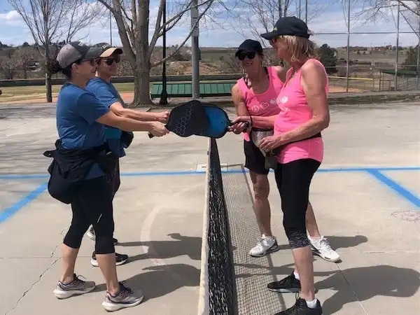 Four people standing on a court, holding pickleball paddles over the net, smiling.