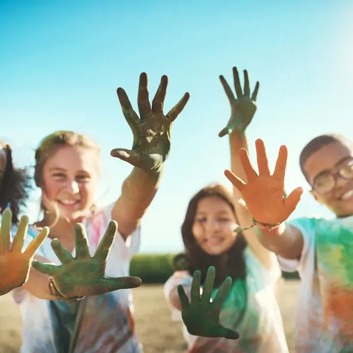 People smiling, showing painted hands outdoors under a clear sky.