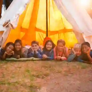 A group of children lying in a row inside a glowing tent, smiling at the camera.