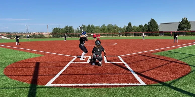 A softball game in progress; pitcher throwing, batter ready, catcher and umpire in position.