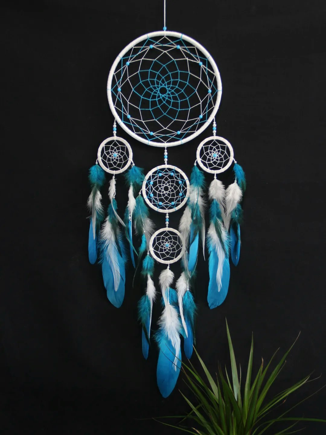 A decorative dreamcatcher with multiple circular frames, blue accents, and feathers, hanging against a black background.