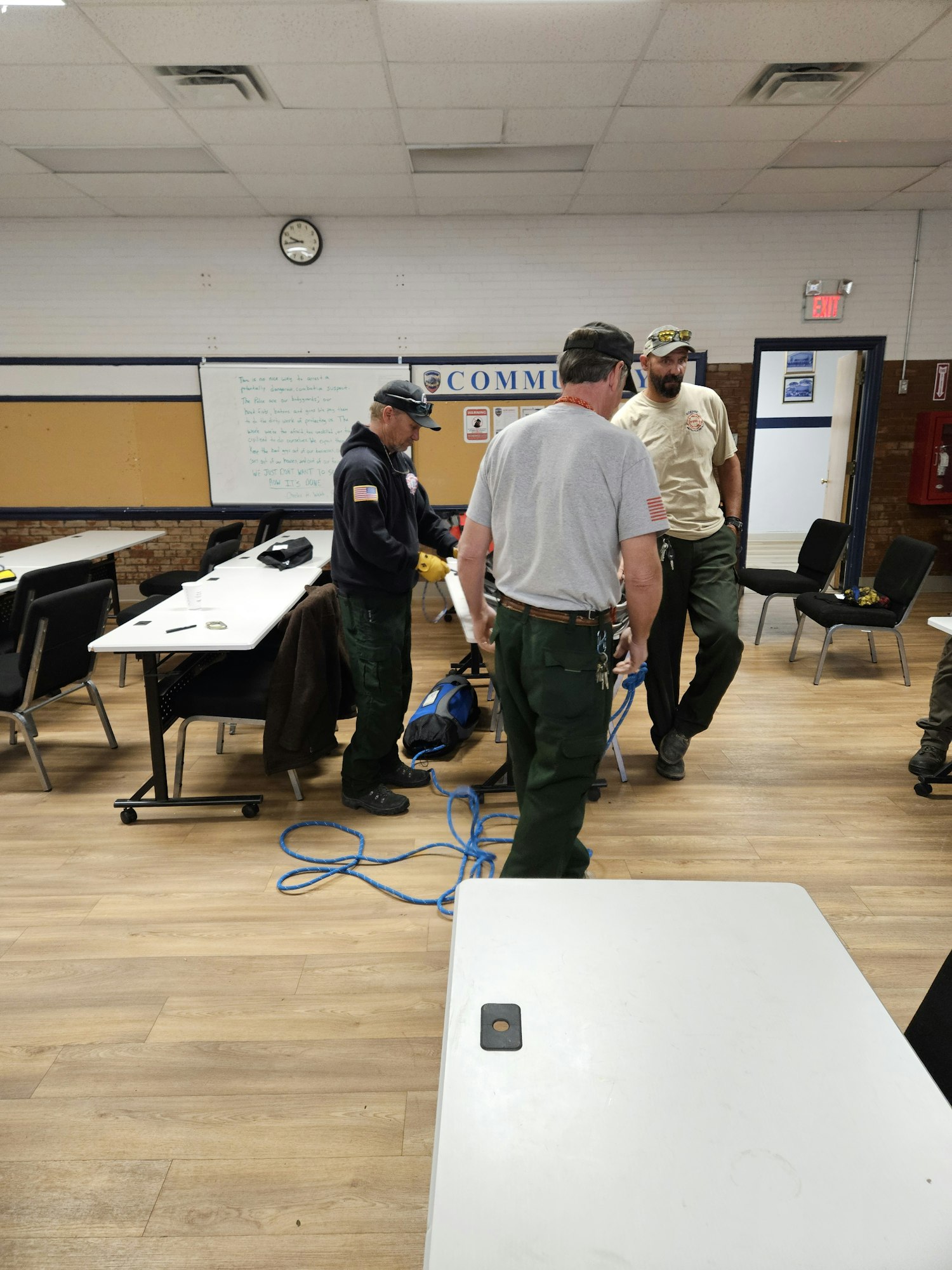 People in a room with tables, some wearing uniforms, holding blue rope.