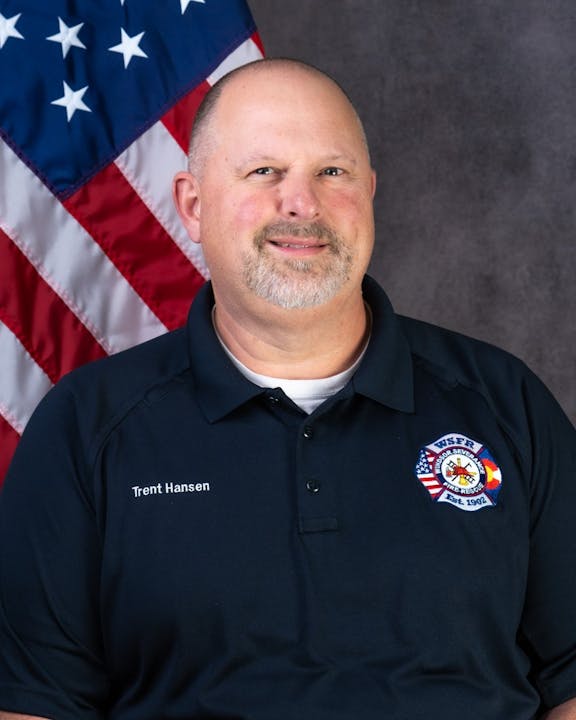 A man in uniform with an American flag backdrop.