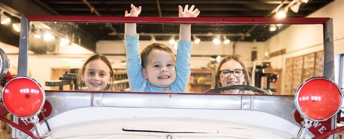 Three children smiling in a vintage firetruck display.