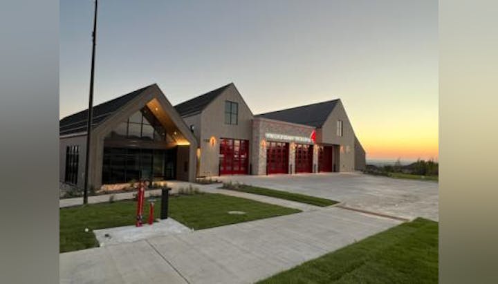 Modern fire station at dusk with red garage doors and a flagpole.
