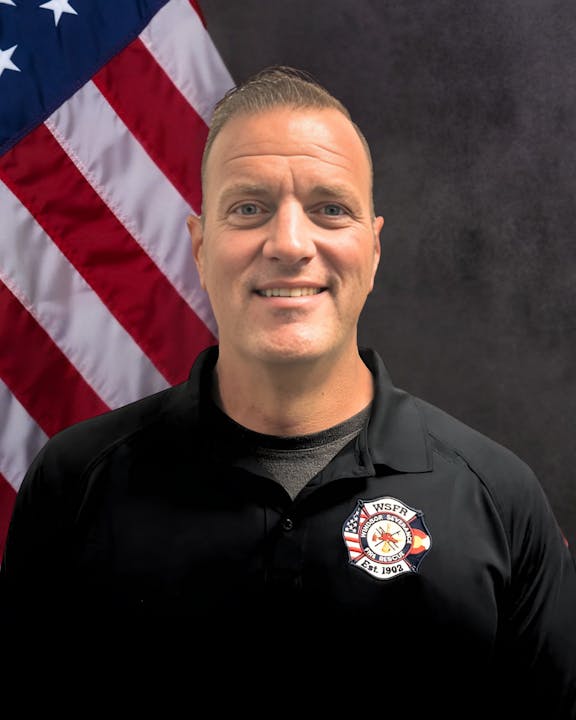 A person in a black shirt with a WSFR logo, standing in front of a U.S. flag.