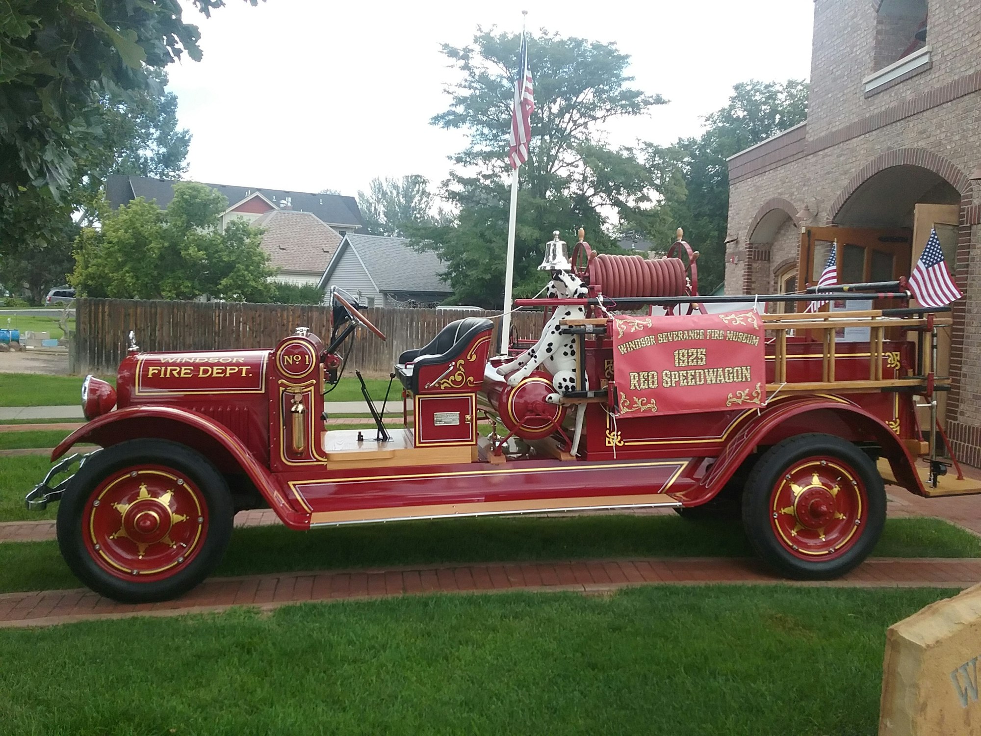 Vintage red fire truck with gold detailing, "Windsor Fire Dept" insignia, and American flags, parked on a driveway.