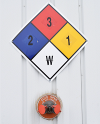 A NFPA 704 diamond hazard sign and a red fire alarm bell on a white wall.