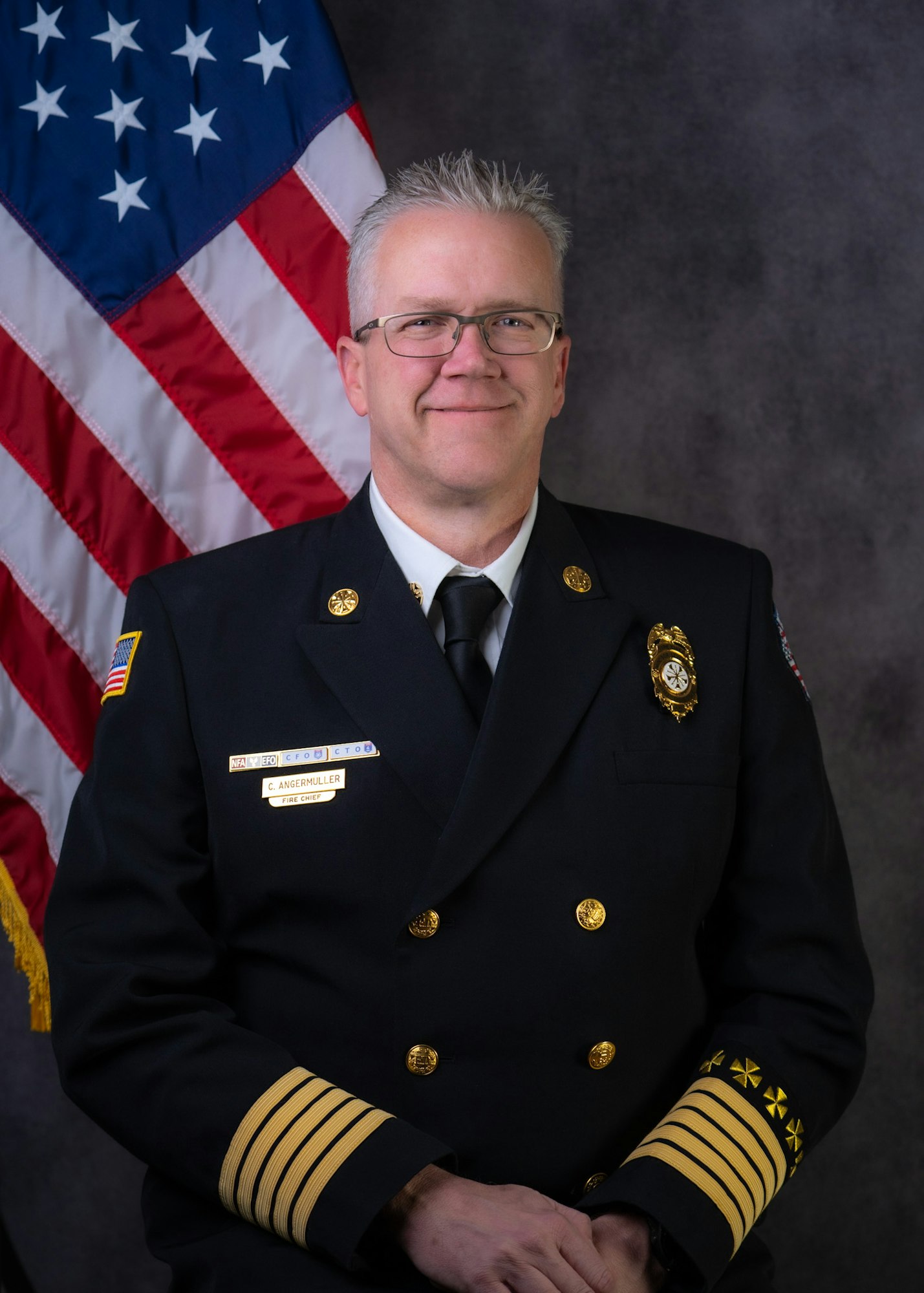 Fire Chief Angermuller in uniform posing before an American flag.